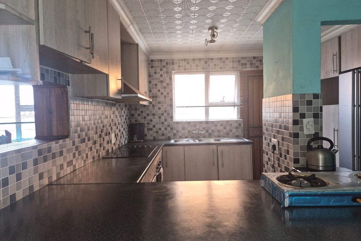 A functional kitchen featuring built-in cabinetry, mosaic tile backsplash, and a breakfast bar, offering a practical layout with potential for modern updates.
