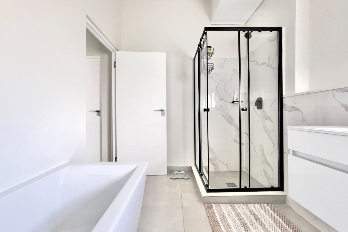 Modern bathroom featuring a sleek walk-in shower with black framing, marble-look wall tiles, a freestanding bathtub, and a contemporary vanity unit.