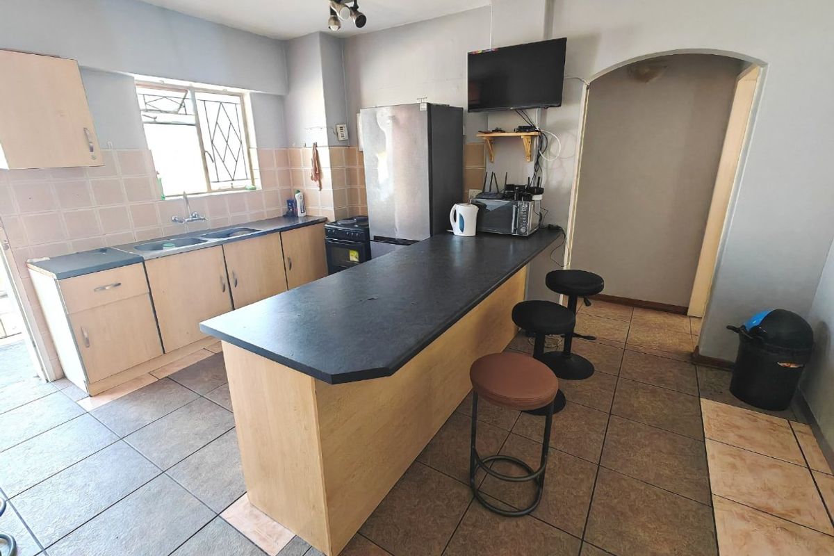 Functional kitchen featuring laminate cabinetry, a breakfast bar, double basin sink, and tiled flooring with a neutral backsplash.