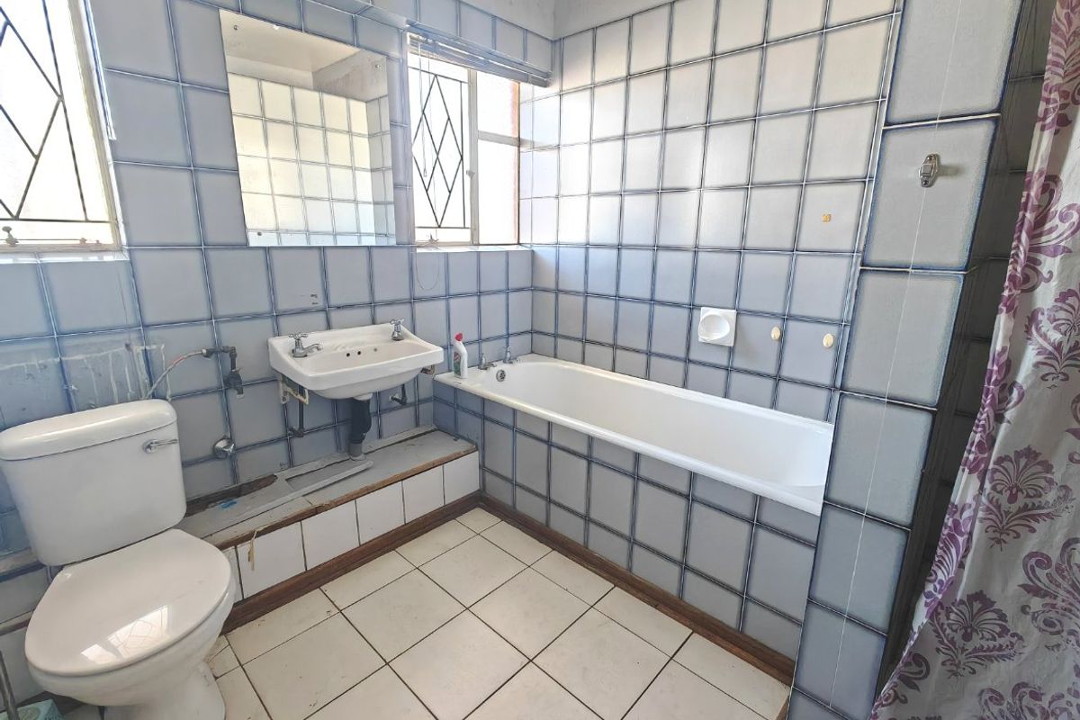 A dated bathroom featuring blue-toned wall tiles, a standard bathtub, wall-mounted basin, and tiled flooring, requiring cosmetic updates to modernize the space.