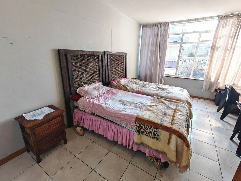 A bedroom featuring tiled flooring and a large window, providing natural light. The space requires cosmetic updates to improve its overall condition.