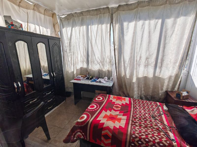 A bedroom featuring tiled flooring and large windows with curtain coverings, offering a functional space with potential for cosmetic updates.
