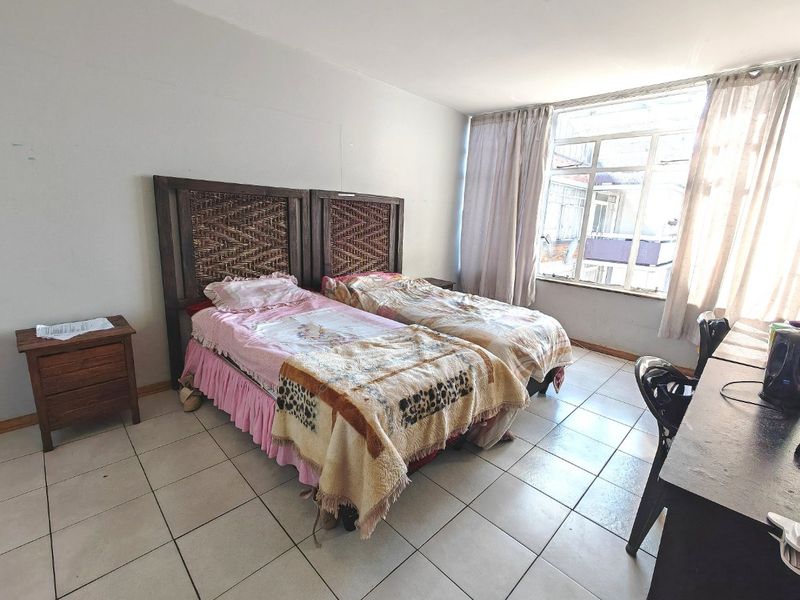 A bedroom featuring tiled flooring and a large window allowing natural light, currently furnished with twin beds.