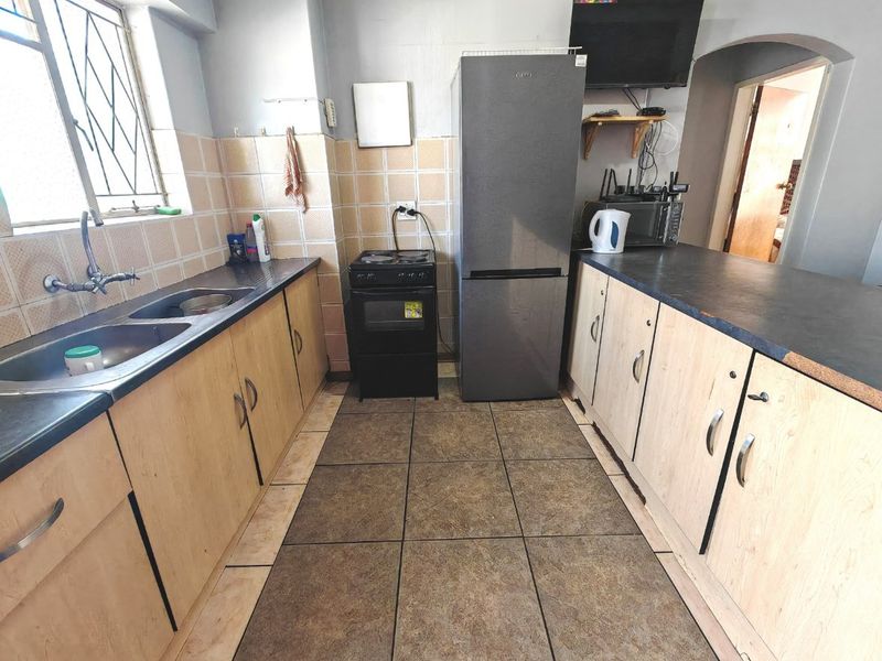A functional kitchen featuring laminate cabinetry, double sink, tiled splashbacks, and ceramic flooring, offering a practical layout with potential for modern updates.