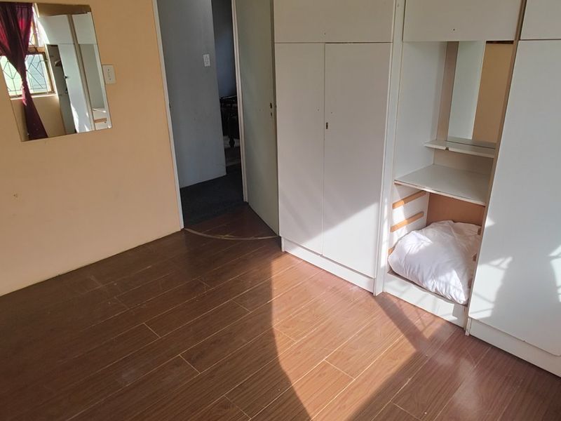 A bedroom featuring tiled flooring and built-in cupboards, offering a functional space with potential for cosmetic updates.