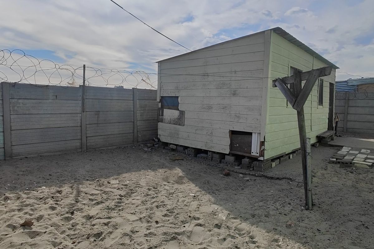 Rear yard area featuring a precast concrete boundary wall with barbed wire and a detached timber-framed structure requiring significant maintenance and repair.