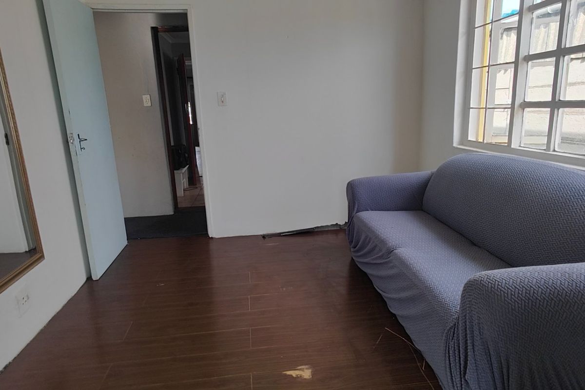 A living room featuring tiled flooring and security bars on the window, currently requiring minor repairs to the flooring and skirting.