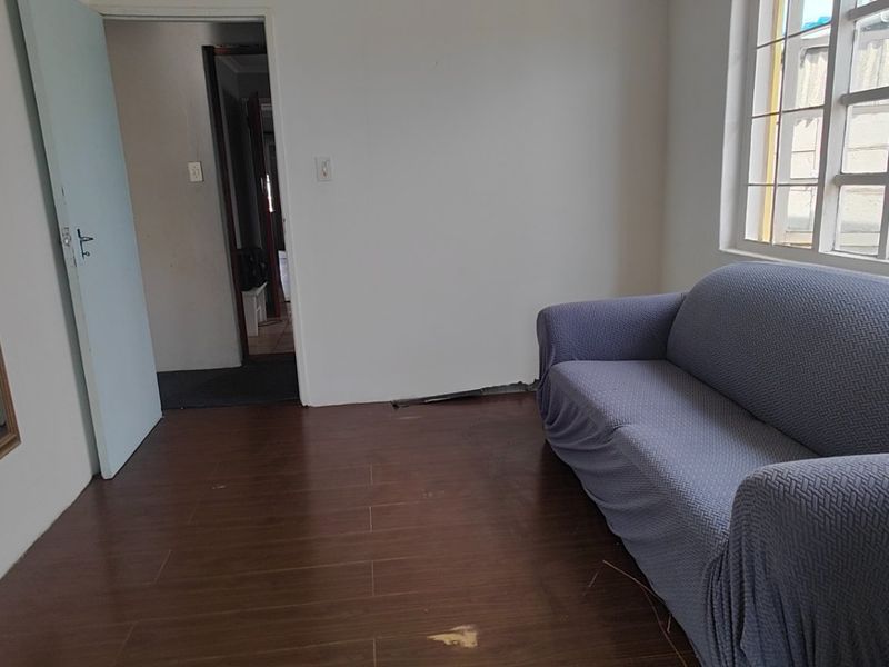 A living room featuring tiled flooring and security bars on the window, currently requiring minor repairs to the flooring and skirting.