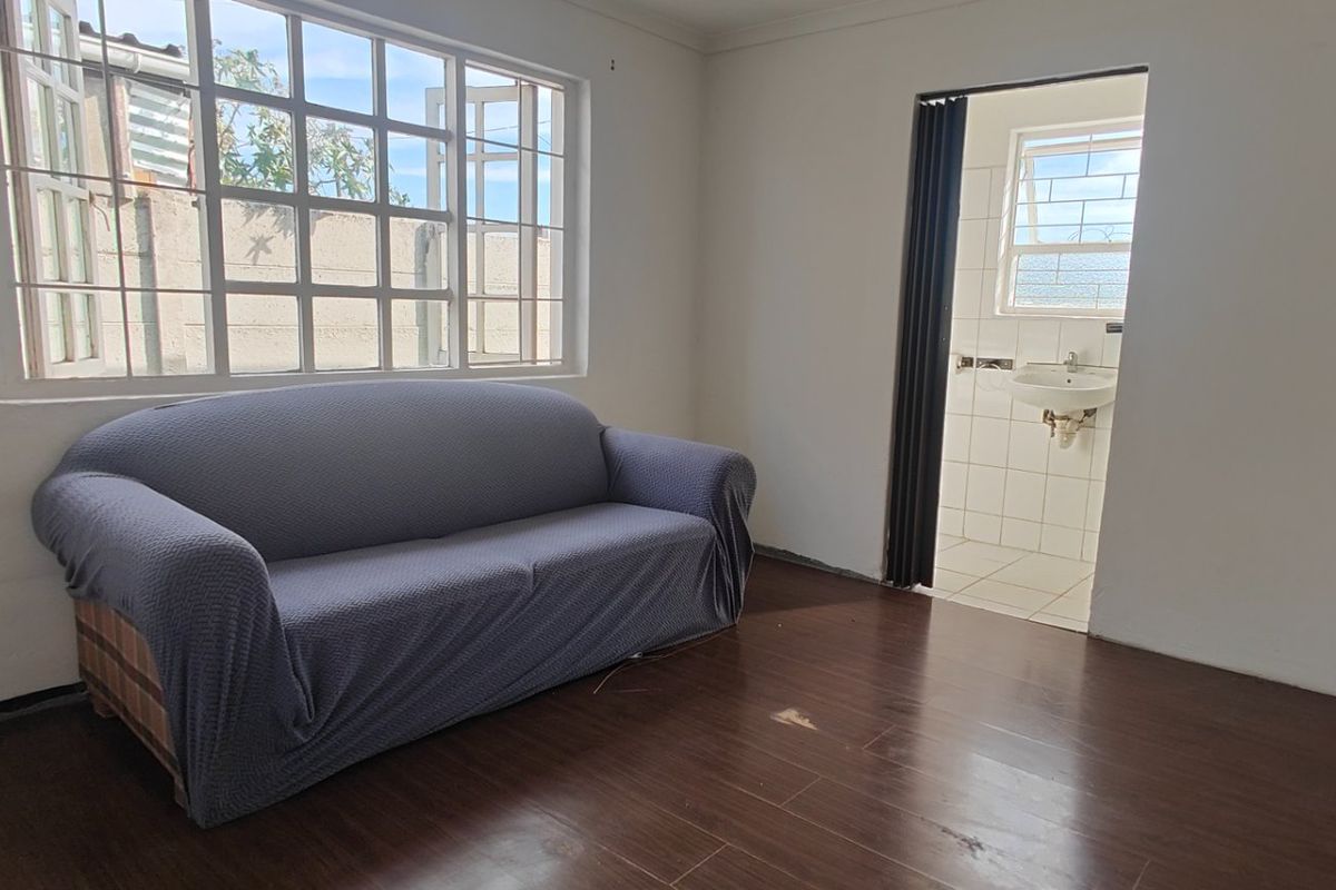 A bedroom featuring laminate flooring, steel-framed windows with security bars, and an attached en-suite bathroom accessed via a folding door.