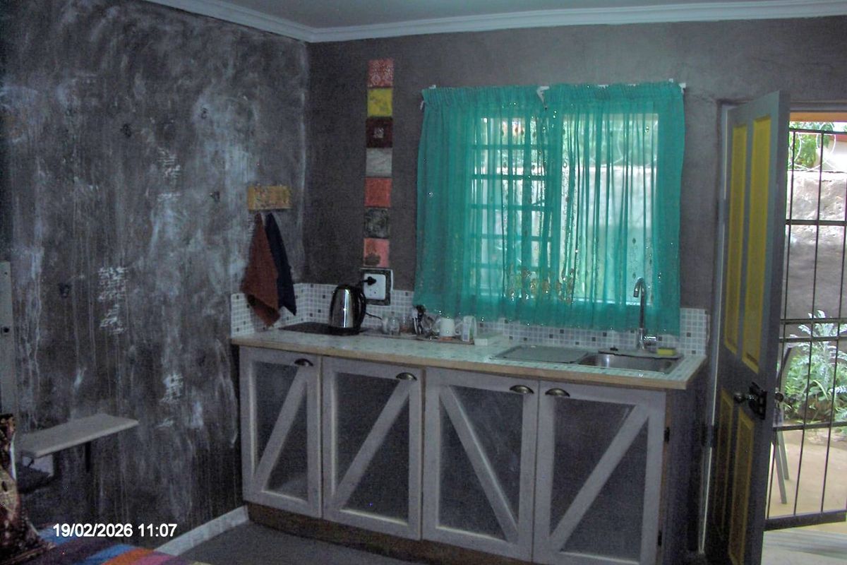 A small kitchen area featuring built-in cabinetry, a stainless steel sink, and a tiled splashback, with direct access to an exterior door.
