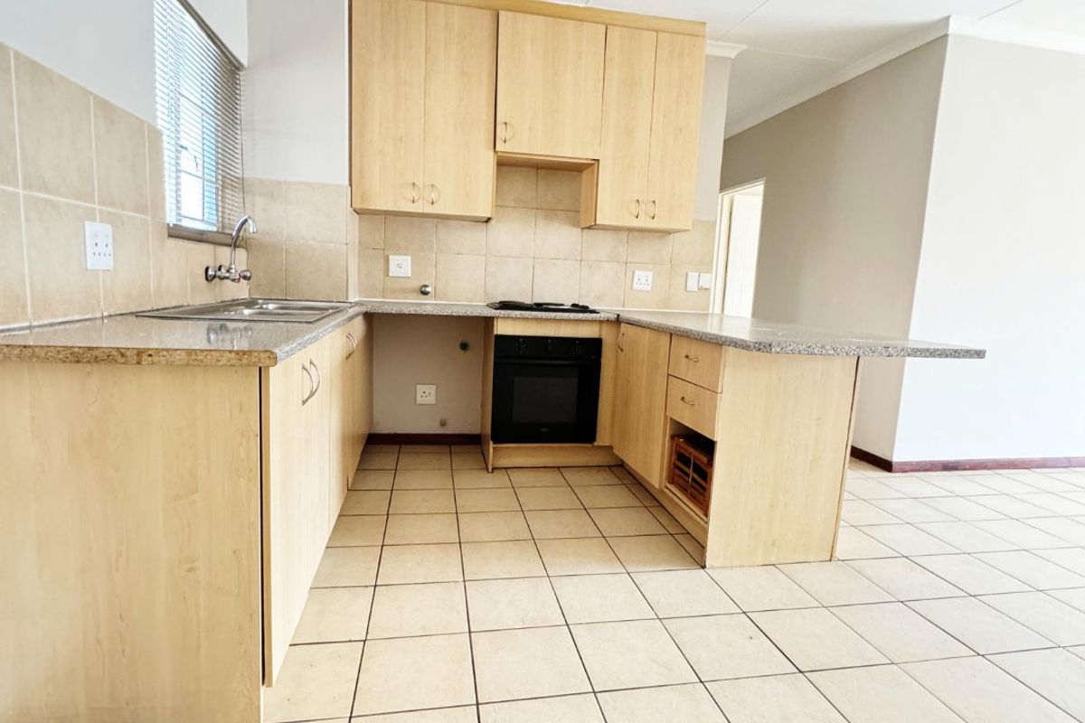 A functional kitchen featuring light wood cabinetry, granite countertops, built-in oven, hob, and tiled flooring in an open-plan layout.