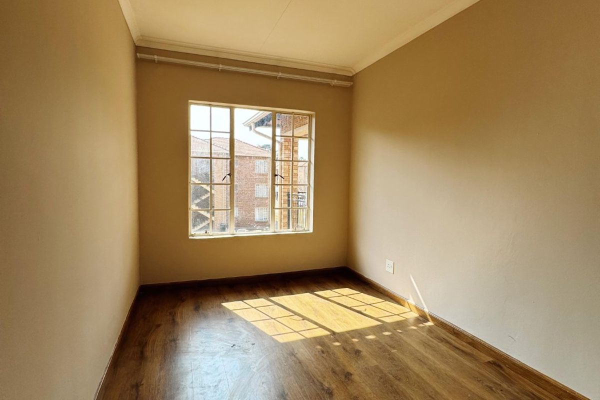 A bright, empty bedroom featuring laminate flooring, neutral walls, and a window with security bars, offering a clean canvas for personalization.