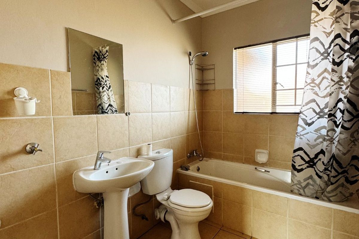 A functional bathroom featuring a pedestal basin, toilet, and a bathtub with a shower attachment, finished with neutral wall and floor tiles.