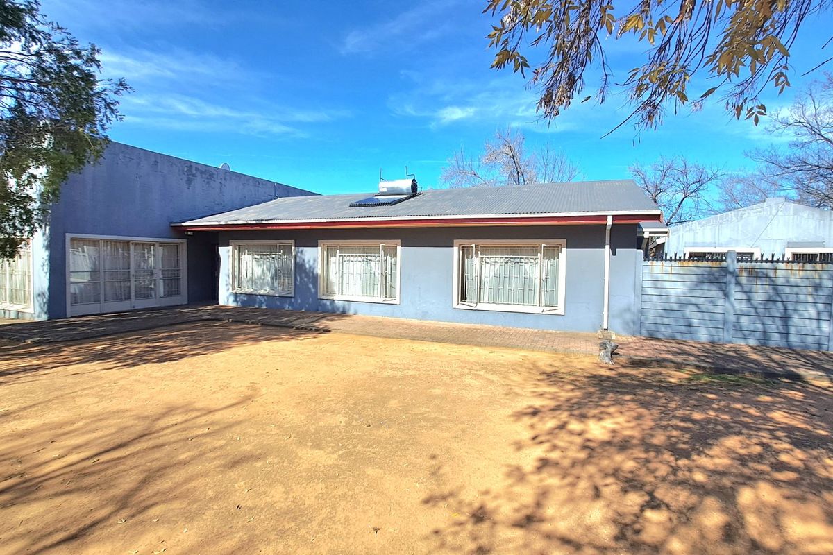 Rear view of the property featuring a corrugated metal roof with a solar water heater, paved patio area, and secure perimeter fencing.