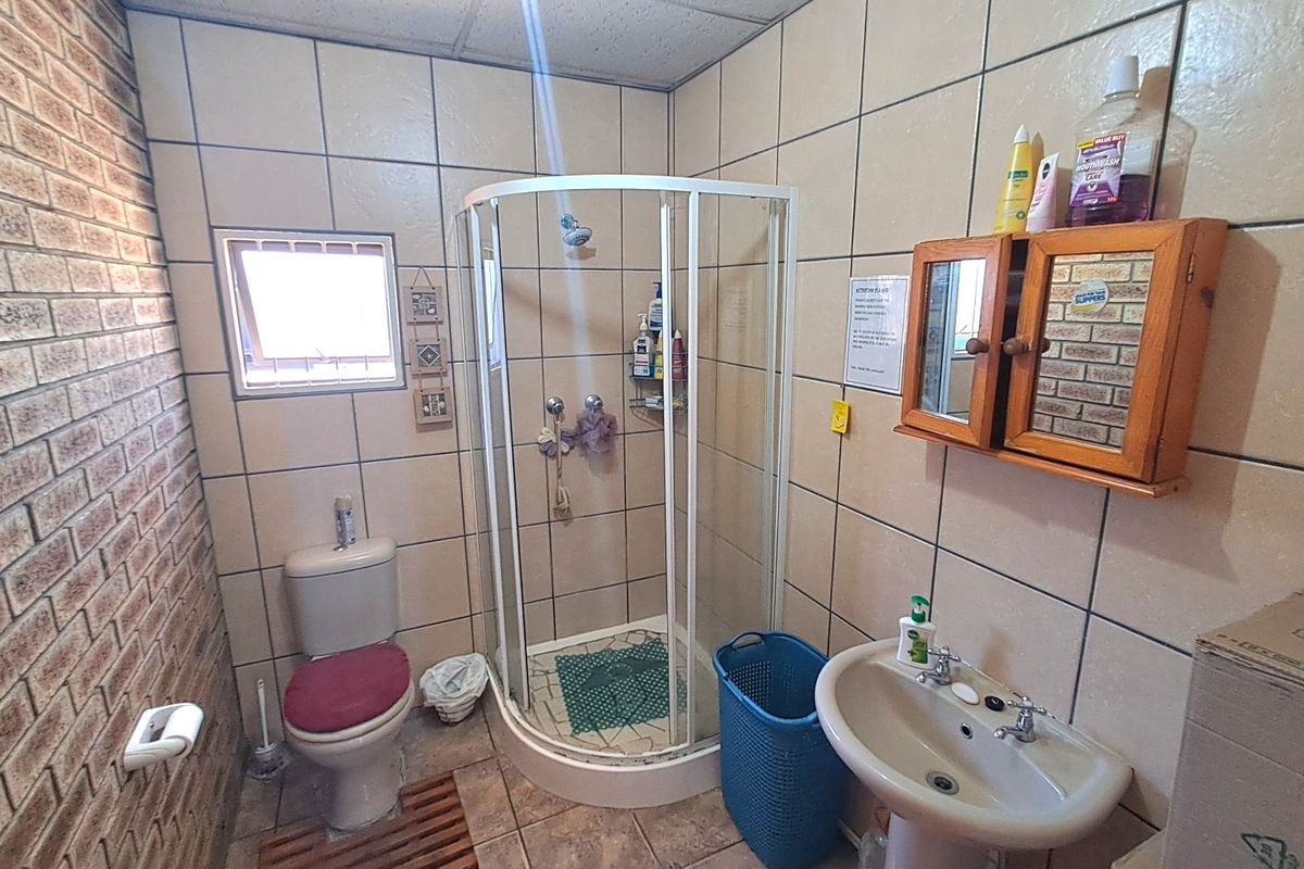 A functional bathroom featuring a corner shower enclosure, pedestal basin, and toilet, finished with tiled walls and flooring.
