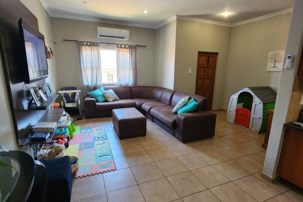 Spacious living room featuring tiled flooring, recessed downlighting, and a wall-mounted air conditioning unit, providing a comfortable and functional family living space.