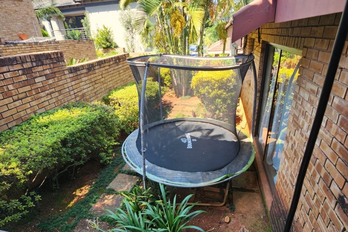 A rear garden area featuring brick boundary walls, established landscaping, and access to the home via a sliding glass door.