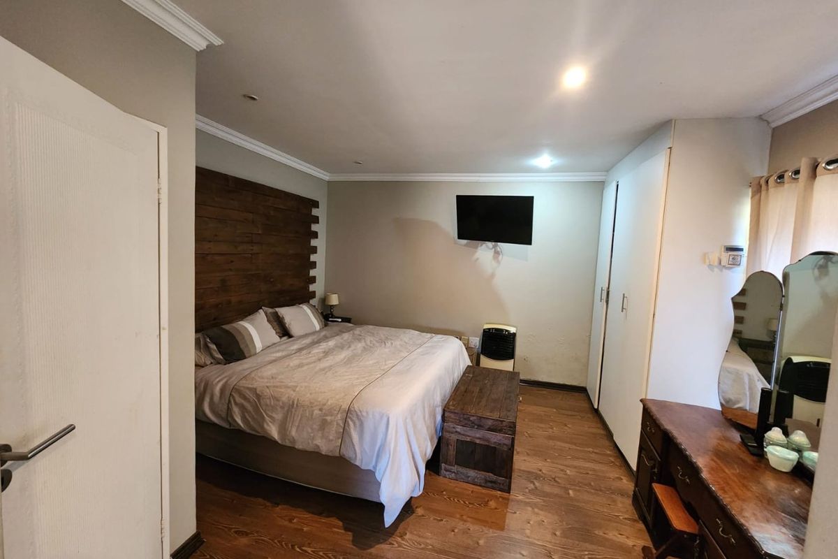 A bedroom featuring timber flooring, built-in wardrobes, and crown molding, offering a functional space with neutral wall tones.