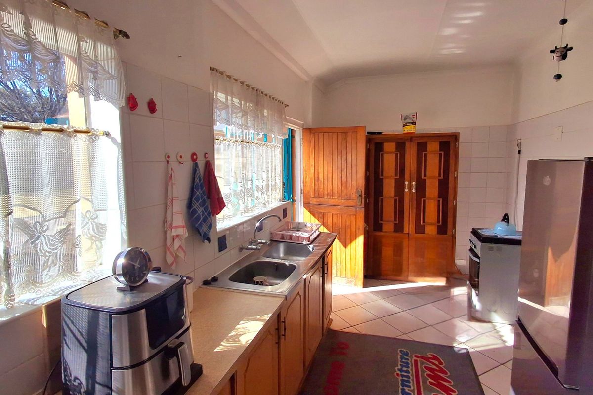 A functional kitchen featuring built-in wooden cabinetry, a double stainless steel sink, tiled splashbacks, and tiled flooring with direct access to an exterior door.