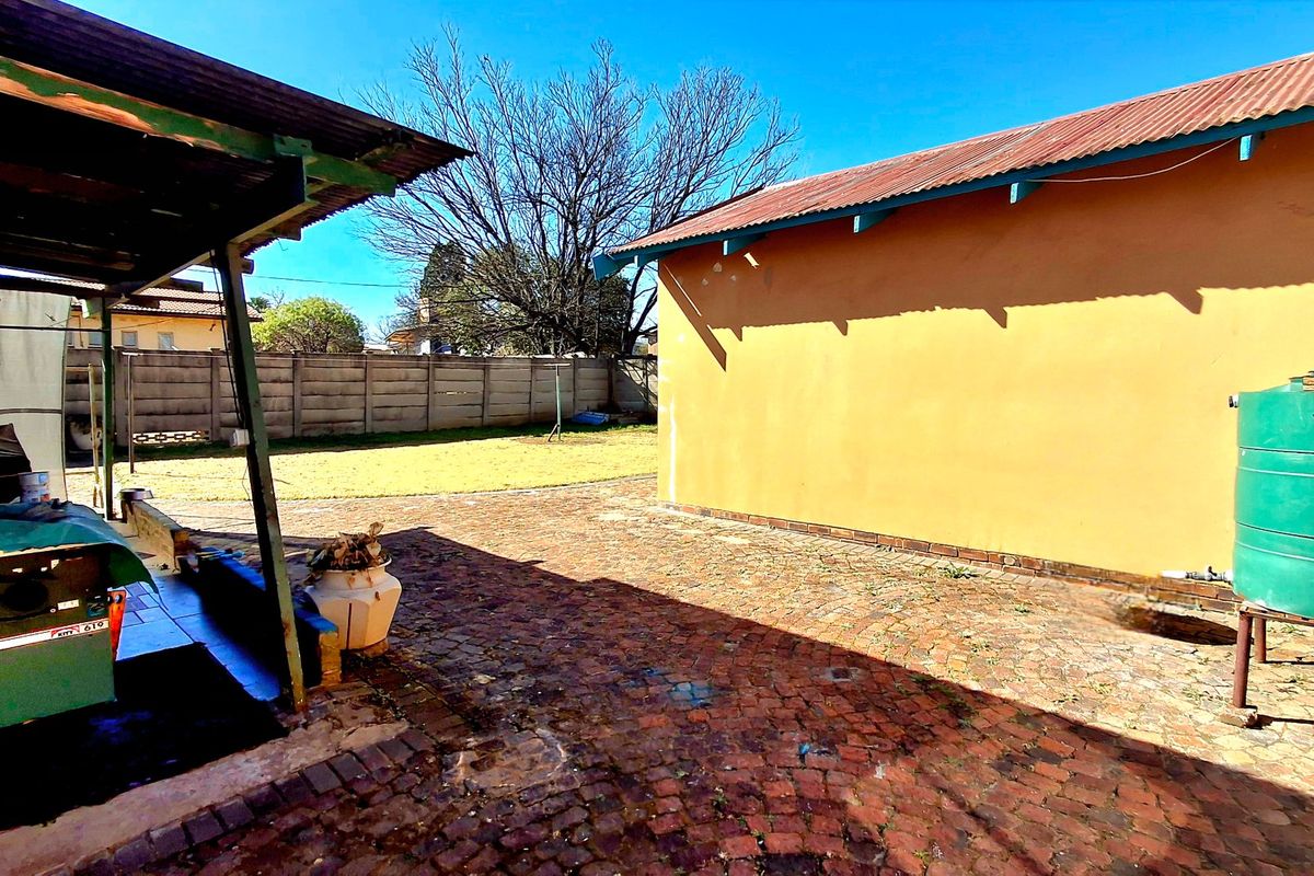 Rear exterior view featuring a covered patio area, brick paving, and a water storage tank set against a precast boundary wall.