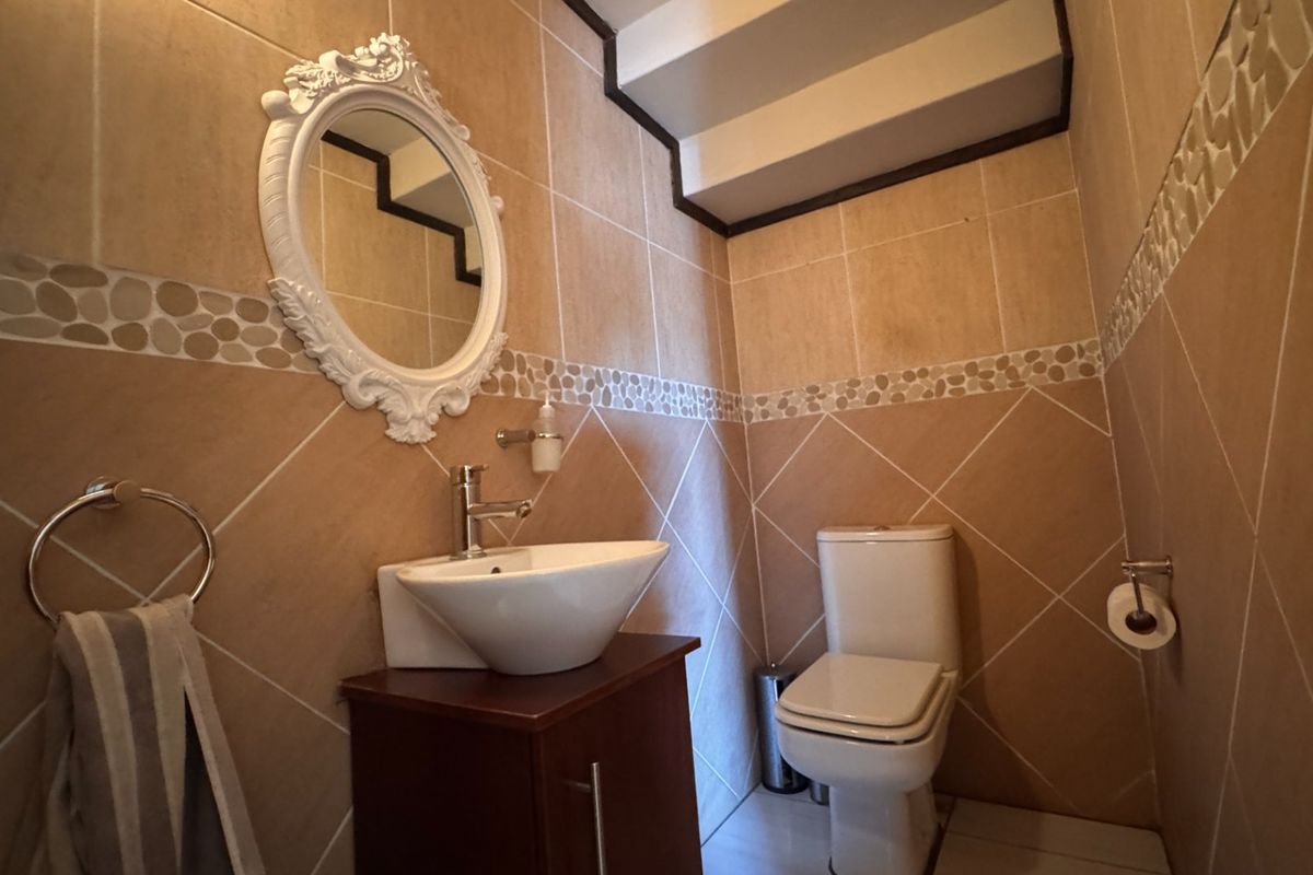 A compact bathroom featuring floor-to-ceiling ceramic tiling, a modern vessel sink with vanity cabinet, and a standard toilet.