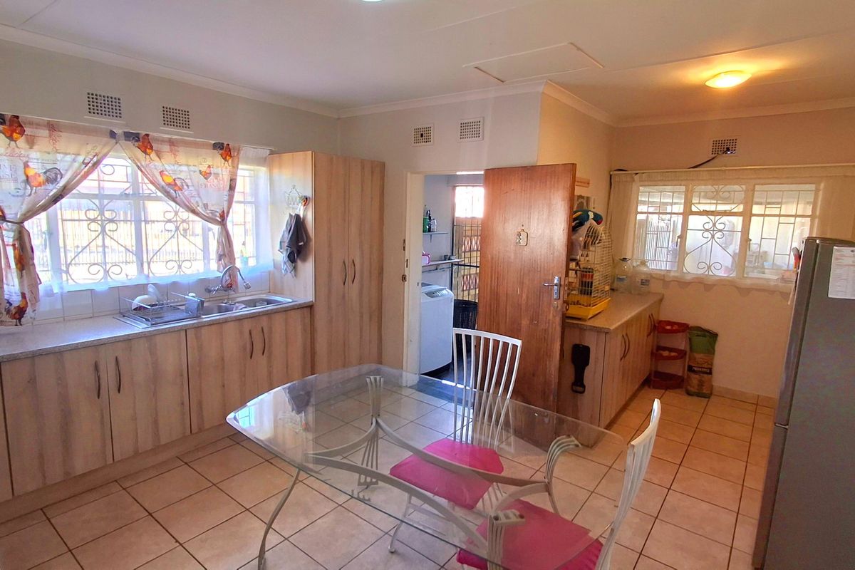 Functional kitchen featuring light wood-look cabinetry, tiled flooring, and a double sink, with an adjacent scullery area visible through the doorway.