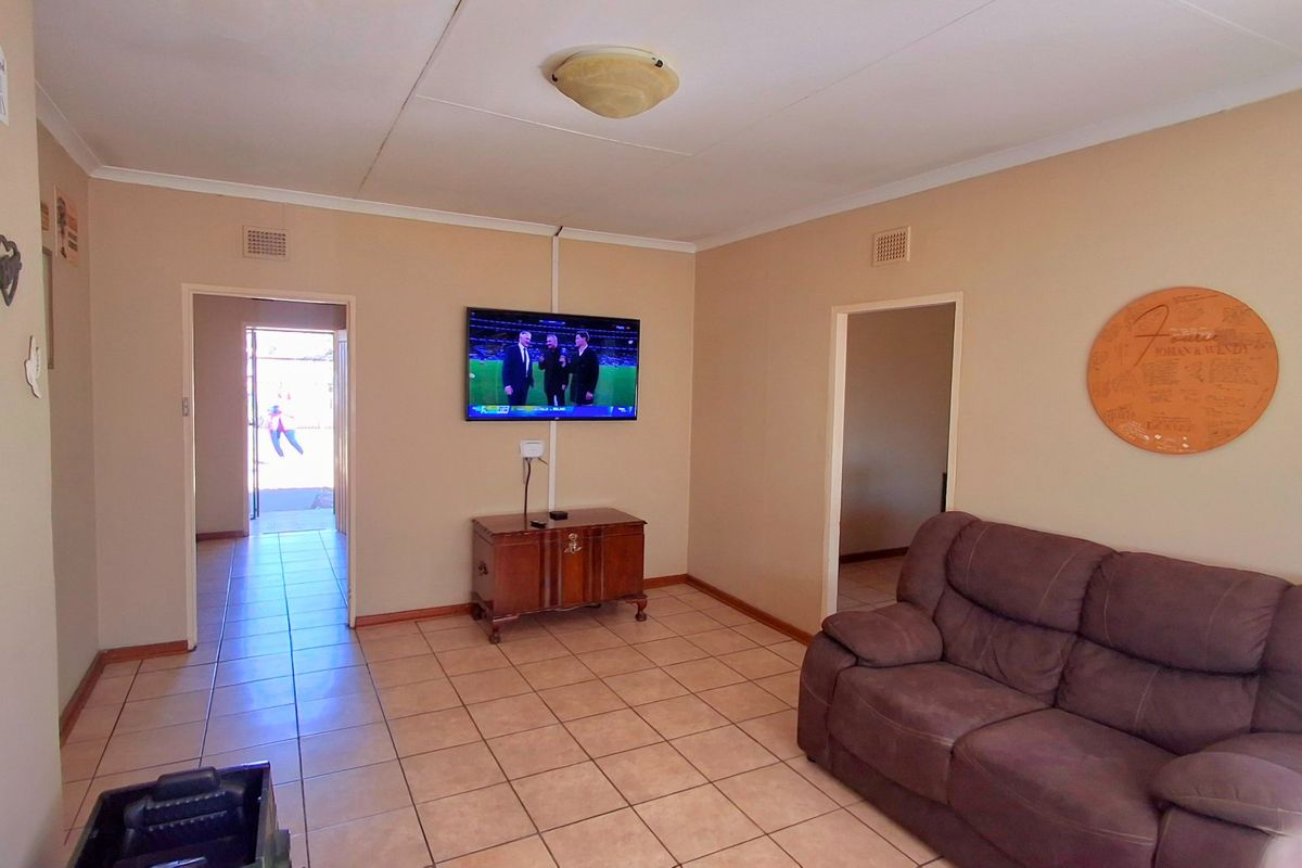 A living room featuring neutral wall tones and tiled flooring, providing a functional space with direct access to adjacent rooms.