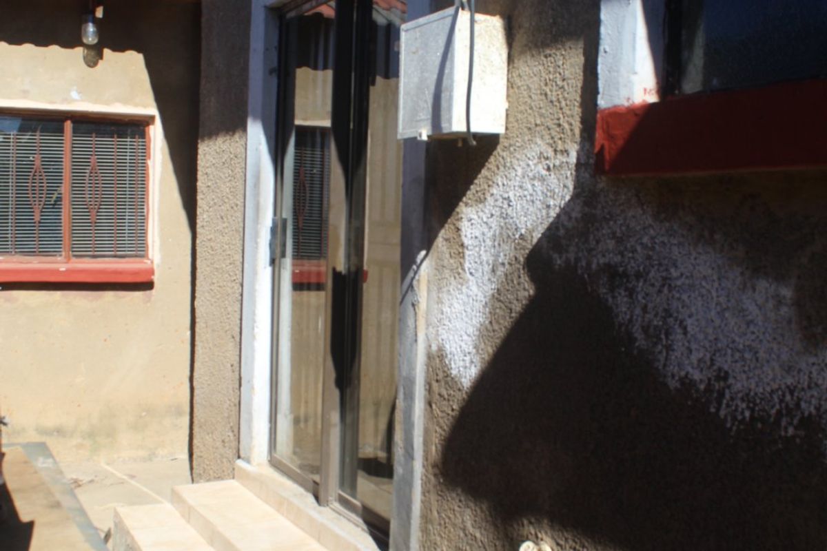 Rear exterior view showing a sliding glass door, tiled entrance steps, and exposed exterior wall finishes with visible plumbing and electrical fixtures.