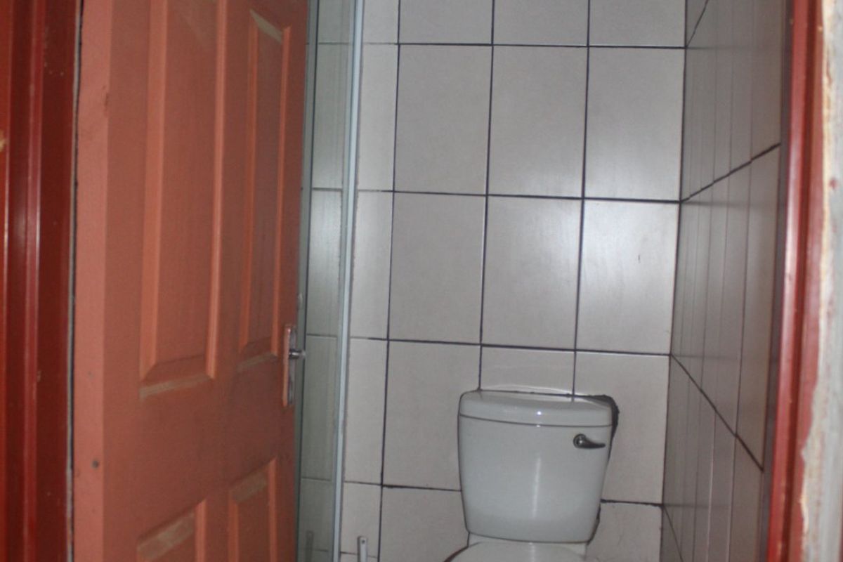 A small bathroom featuring a toilet and shower enclosure with tiled walls and flooring, currently requiring maintenance and cosmetic updates.