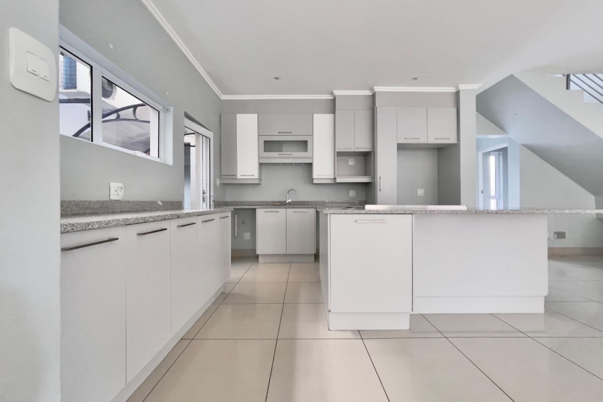 A modern, clean, and empty kitchen featuring neutral cabinetry, granite countertops, tiled flooring, and ample storage space, ready for personalization.
