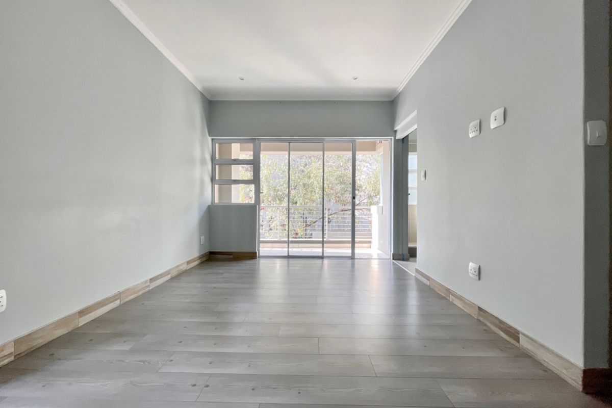 A bright, empty living room featuring modern laminate flooring, recessed lighting, and a large sliding glass door leading to an outdoor balcony.