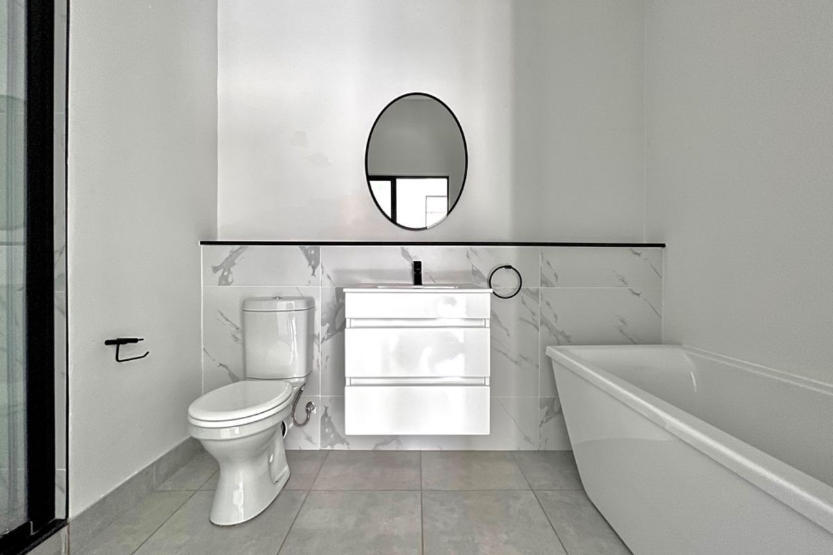 Modern bathroom featuring a sleek wall-mounted vanity, freestanding bathtub, contemporary toilet, and elegant marble-look wall tiling with high-quality finishes.