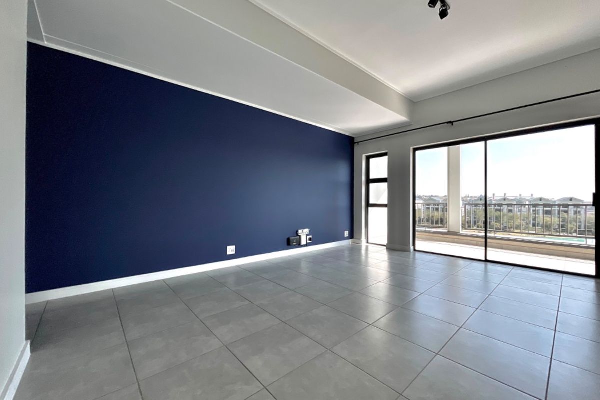 Spacious living area featuring large format floor tiles, a bold navy accent wall, and sliding glass doors leading to a private balcony.