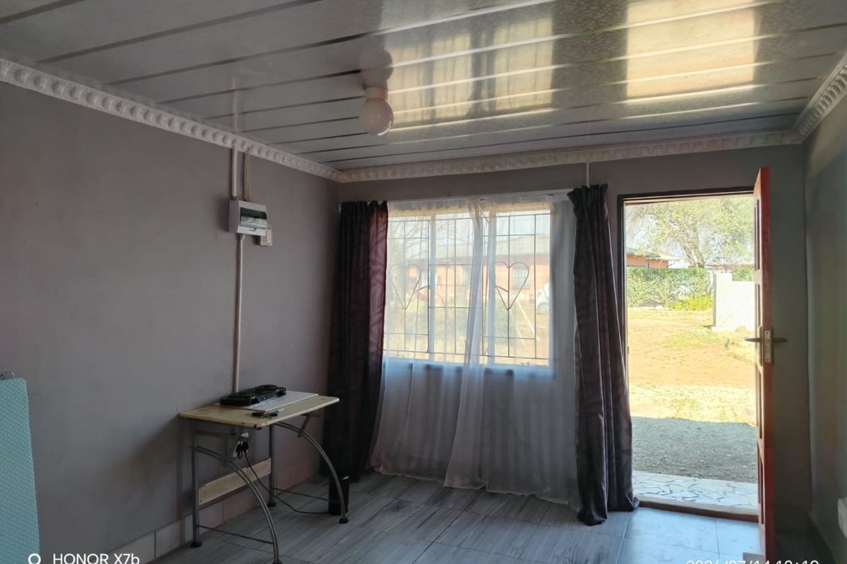 A living area featuring tiled floors, decorative ceiling cornices, and direct access to the exterior, with visible electrical conduit and security window bars.