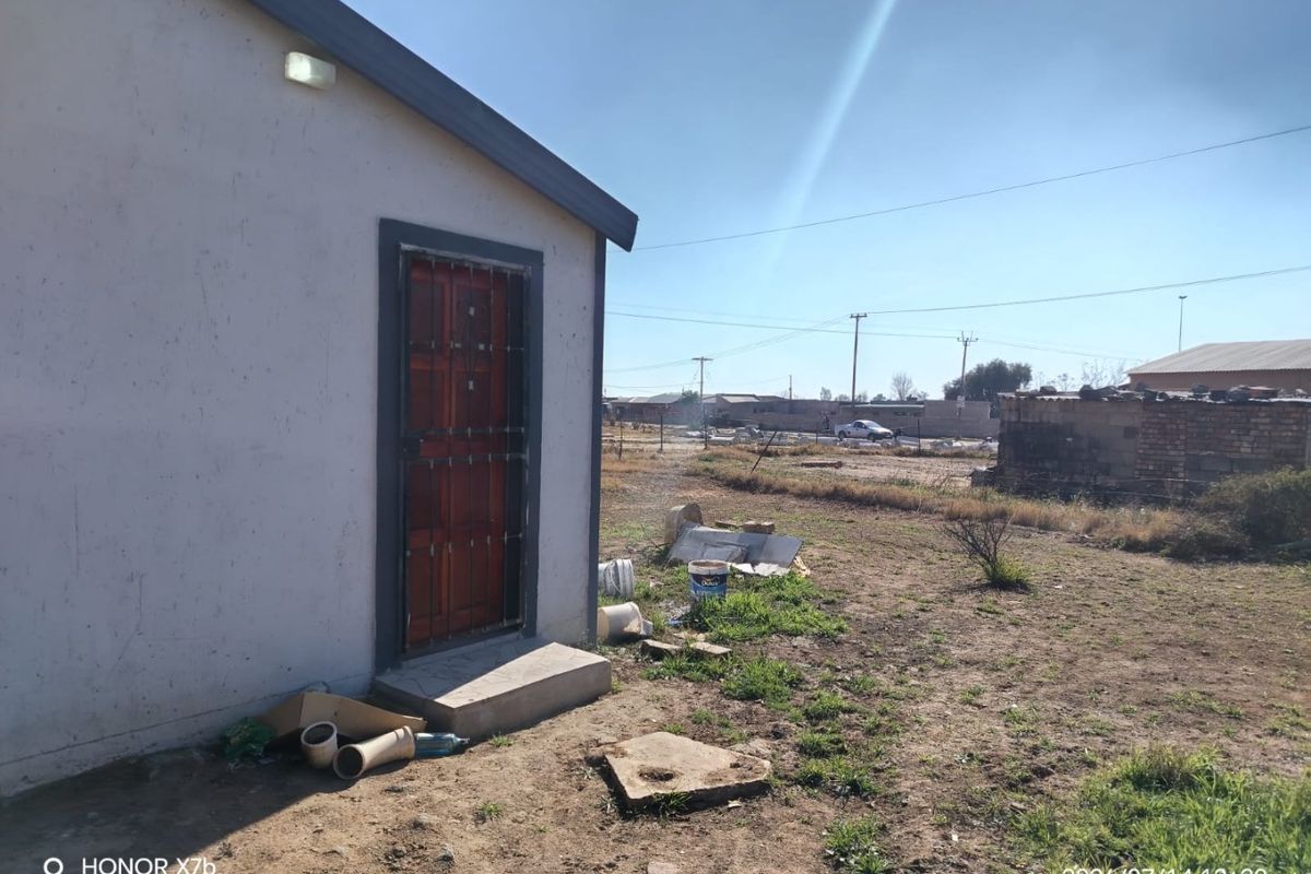 Rear exterior view of the property showing a side entrance with a security gate and an undeveloped yard area.