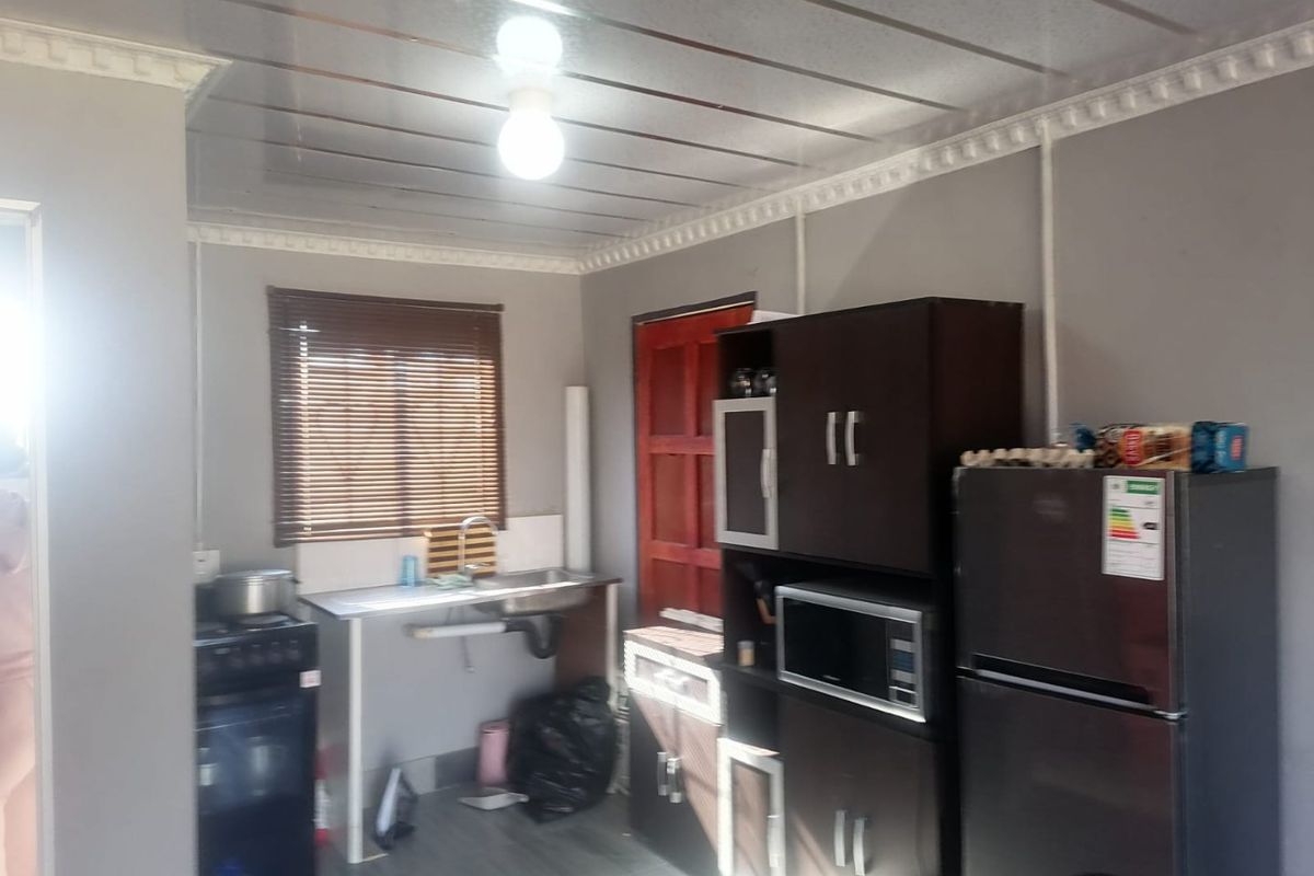 A compact kitchen area featuring dark cabinetry, a stainless steel sink, and venetian blinds, requiring some cosmetic updates to improve the overall finish.