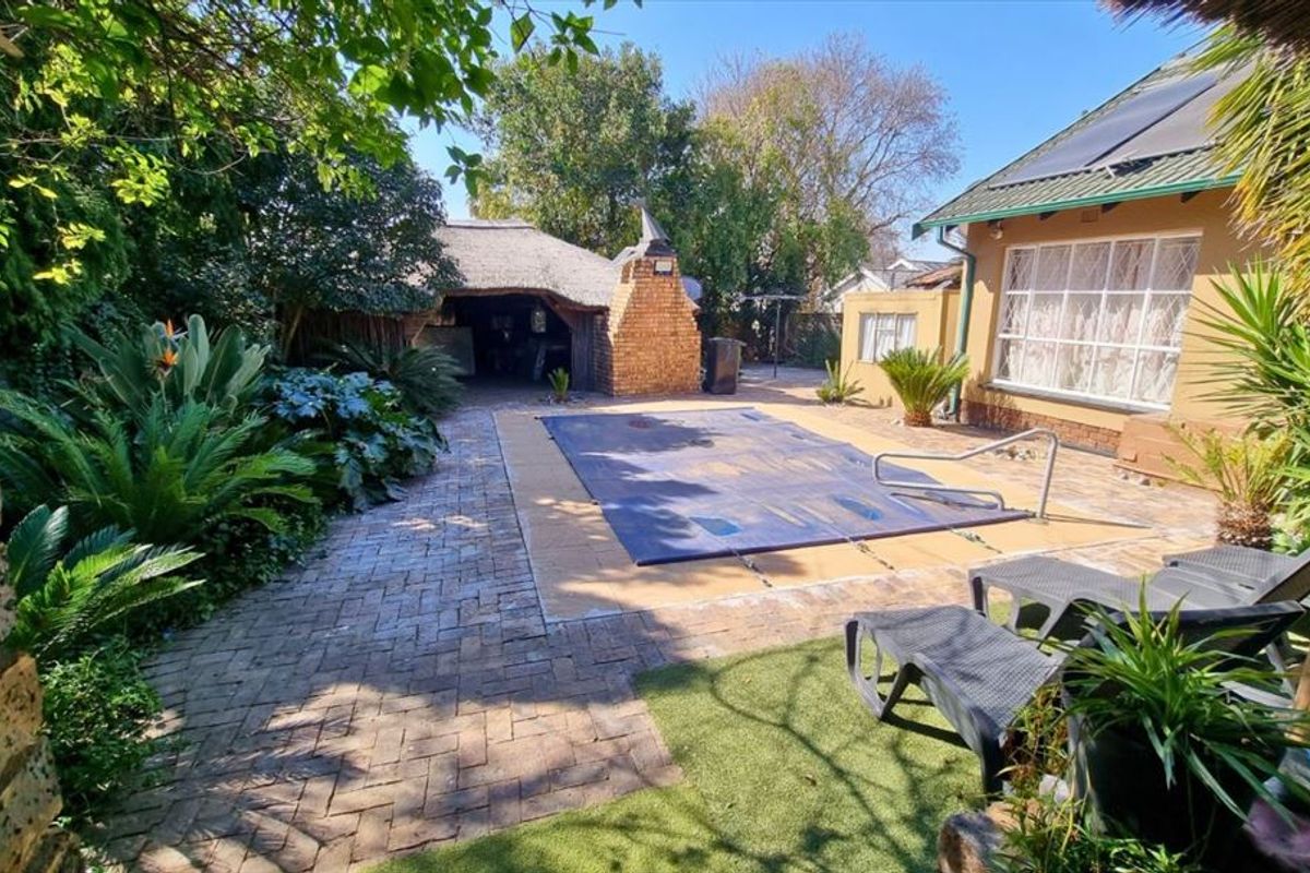 Outdoor entertainment area featuring a swimming pool with cover, paved patio, and a traditional thatched lapa with a built-in brick braai.