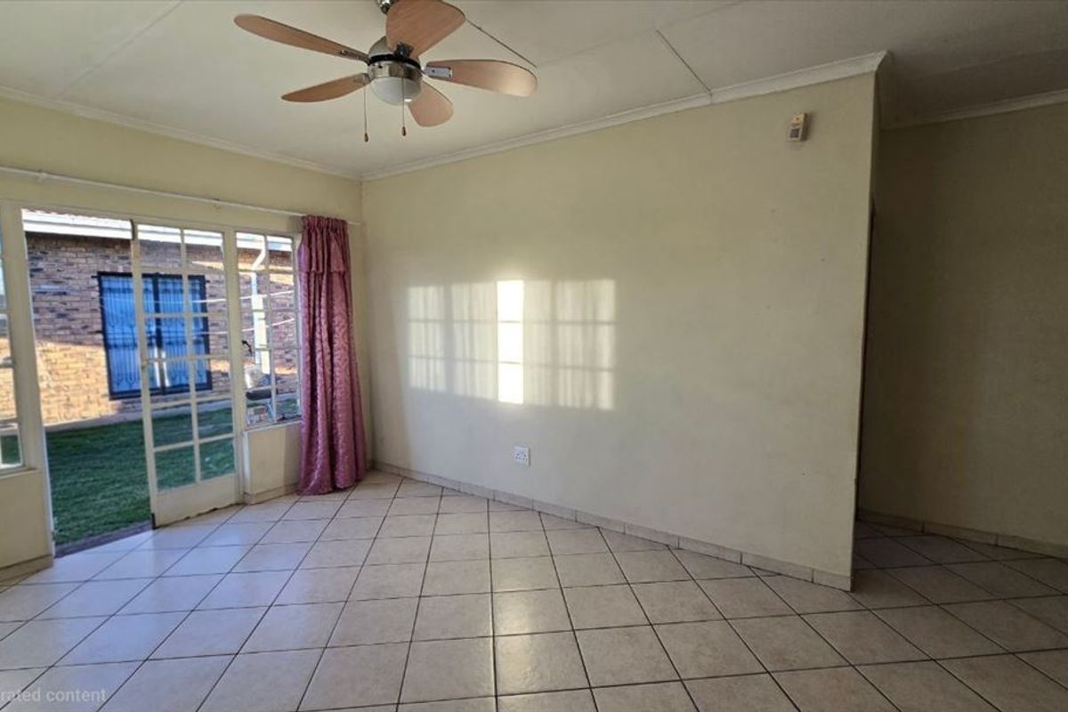 A bright, empty living room featuring tiled flooring, a ceiling fan, and large french doors providing access to the garden area.