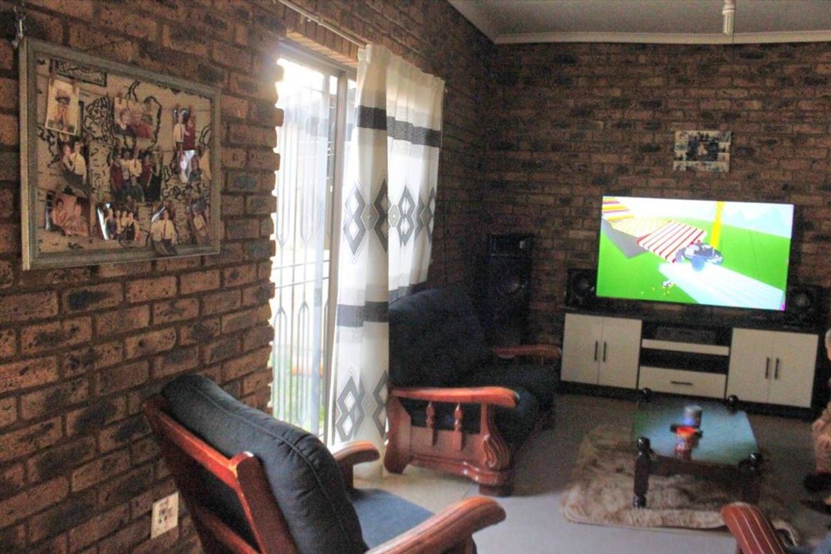 A living room featuring exposed brick walls and a sliding glass door with security gate, providing access to the exterior.