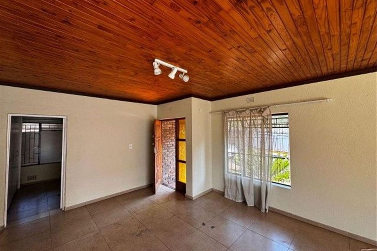 An empty living room featuring a timber-clad ceiling, tiled flooring, and security bars on the windows, offering a blank canvas for renovation.