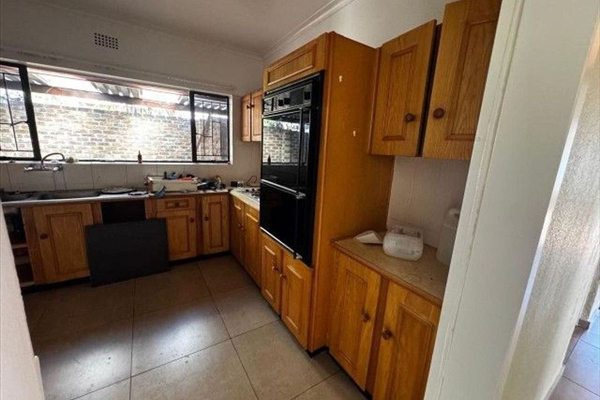 A dated kitchen featuring wooden cabinetry, a double eye-level oven, and tiled flooring, offering significant potential for a modern renovation.
