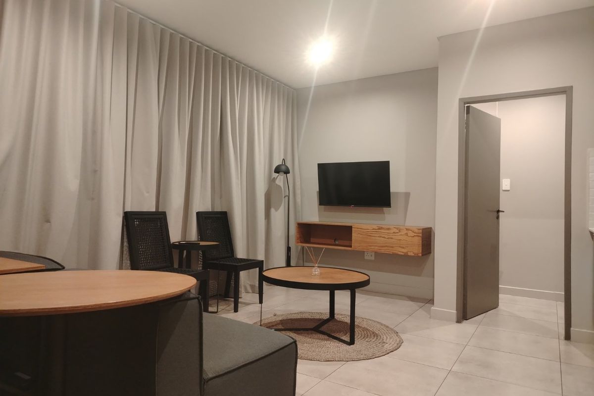 A modern living room featuring tiled flooring, recessed lighting, and a wall-mounted media console, complemented by full-height curtains.