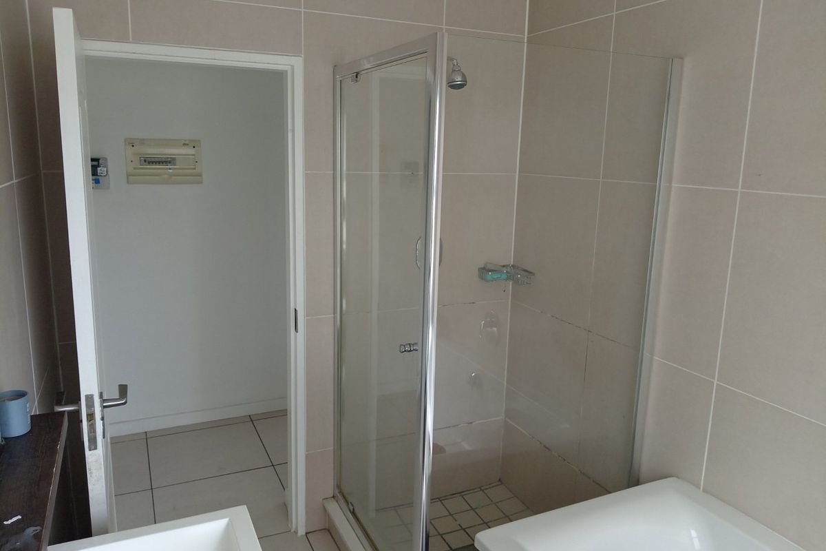 A functional bathroom featuring a glass-enclosed shower, neutral wall tiling, and an adjacent utility area containing the electrical distribution board.