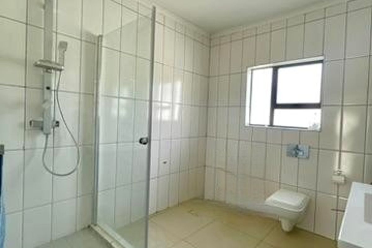 A functional bathroom featuring a glass shower enclosure, wall-hung toilet, and neutral tiled finishes throughout.
