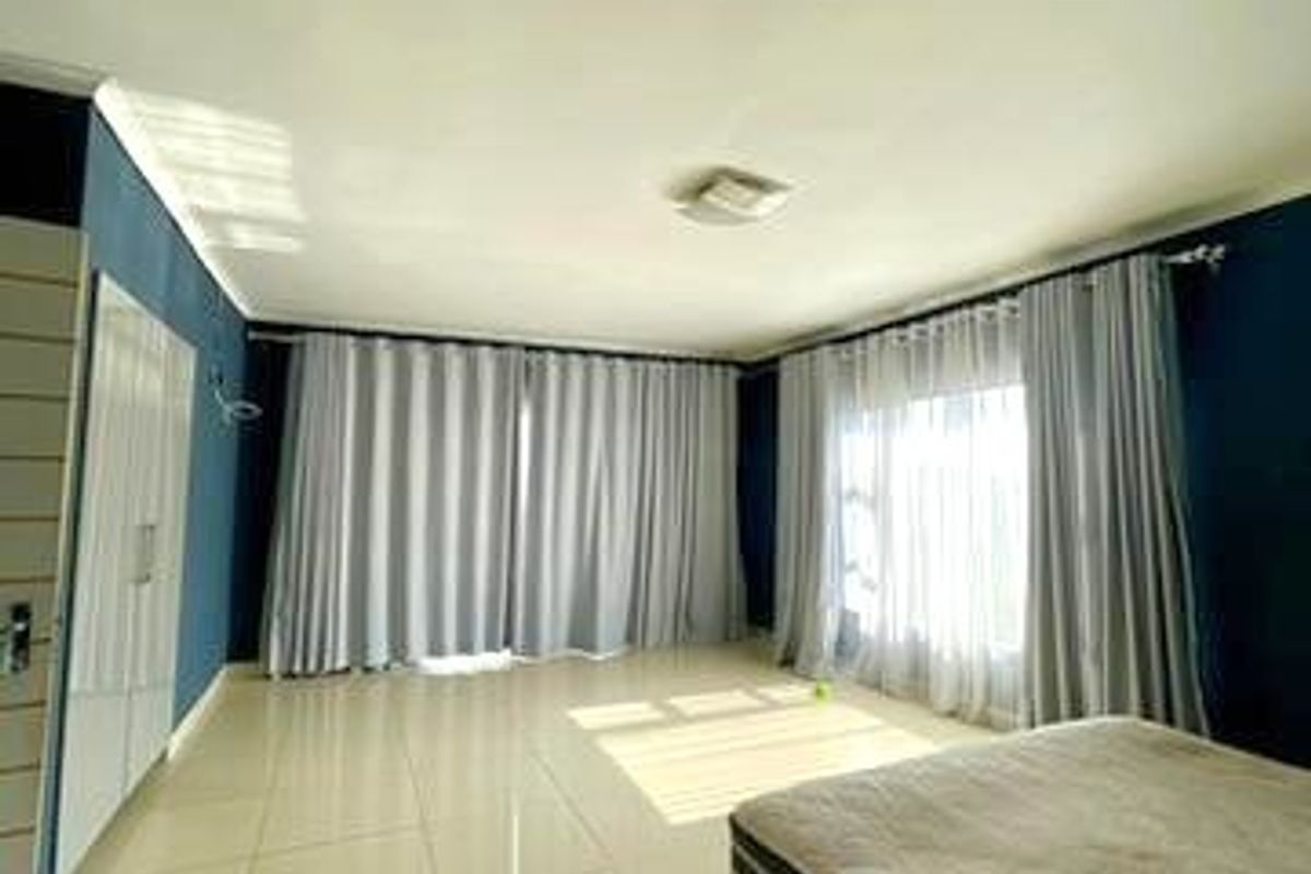 Spacious bedroom featuring large windows with floor-to-ceiling curtains, neutral tiled flooring, and built-in storage cupboards.