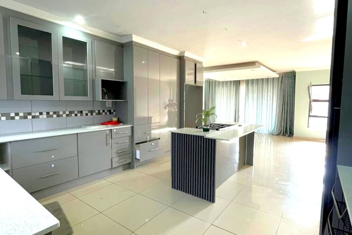 Modern open-plan kitchen featuring high-gloss grey cabinetry, a central island with a built-in hob, stone countertops, and large format floor tiles.