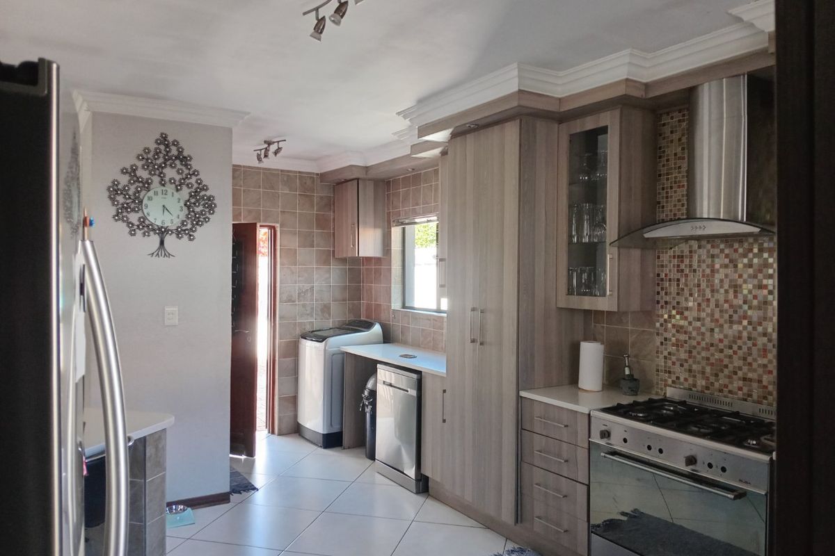 A functional kitchen featuring wood-finish cabinetry, a gas stove with extractor fan, tiled backsplash, and tiled flooring with an adjacent laundry area.