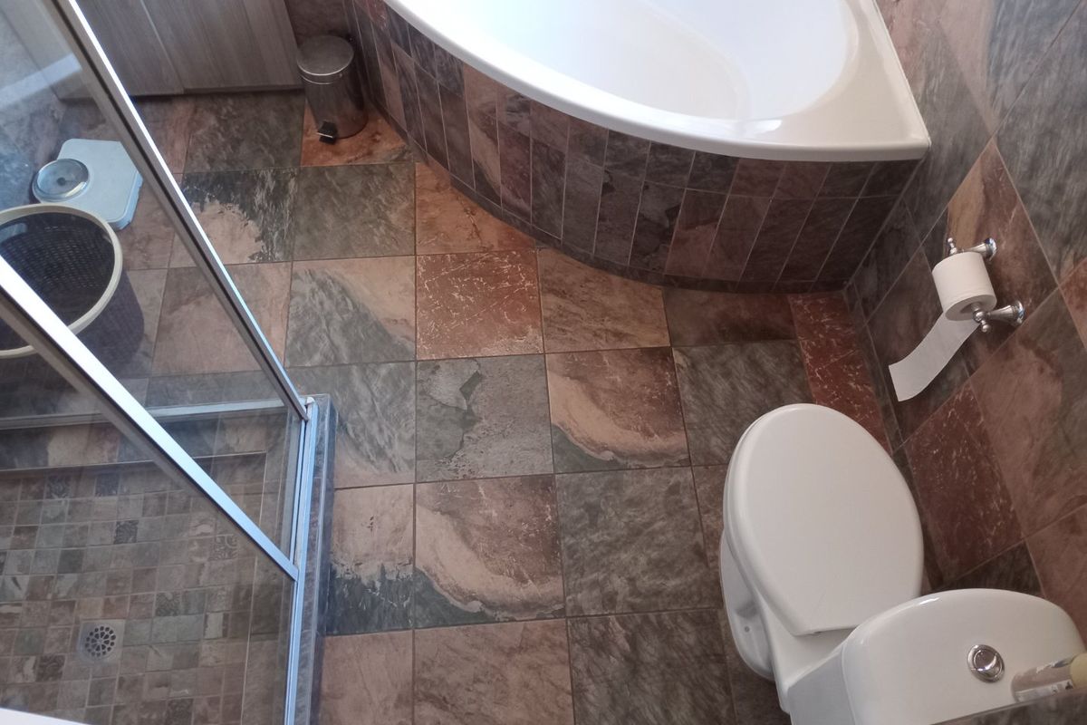 A functional bathroom featuring a built-in corner bathtub, a glass-enclosed shower, and natural stone-look floor and wall tiling.