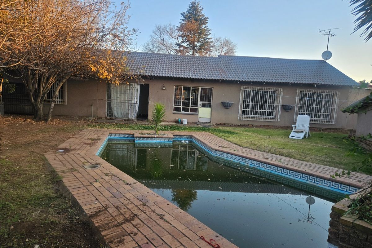 Rear view of the house featuring a swimming pool with brick coping, a tiled roof, and security bars on the windows.