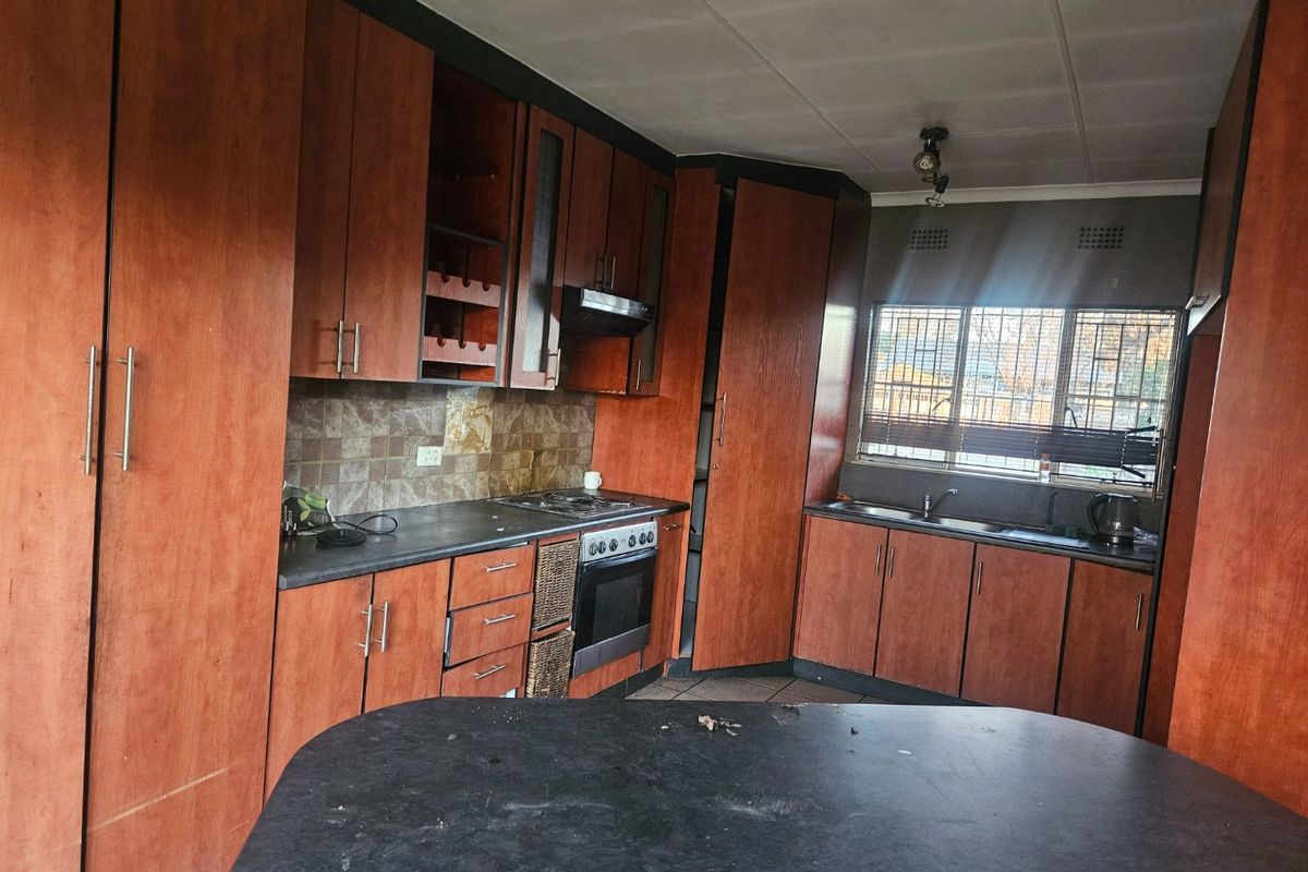 A dated kitchen featuring wood-tone cabinetry, dark laminate countertops, built-in oven, hob, and a double sink with a tiled backsplash.